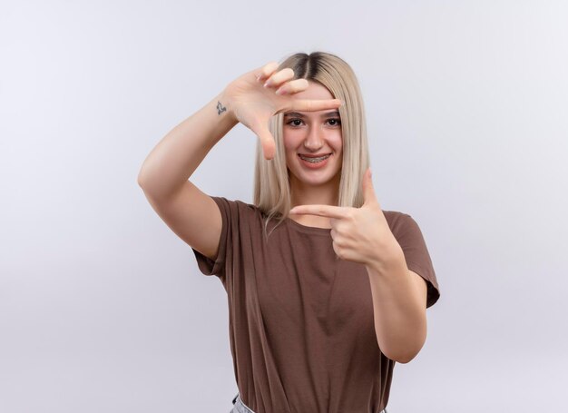 Souriante jeune fille blonde dans un appareil dentaire faisant des gestes cadre sur un espace blanc isolé avec copie espace