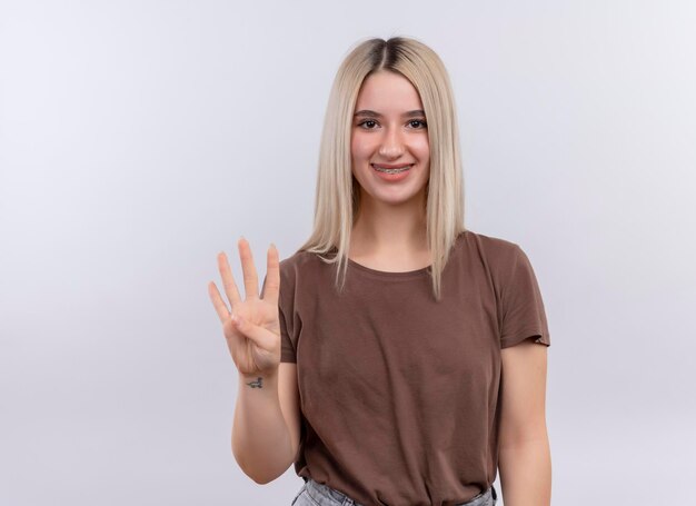 Souriante jeune fille blonde dans un appareil dentaire montrant quatre sur un espace blanc isolé avec copie espace