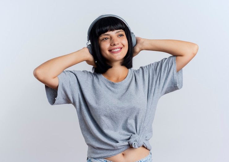 Photo gratuit souriante jeune fille brune caucasienne sur les écouteurs met les mains sur la tête derrière isolé sur fond blanc avec espace de copie