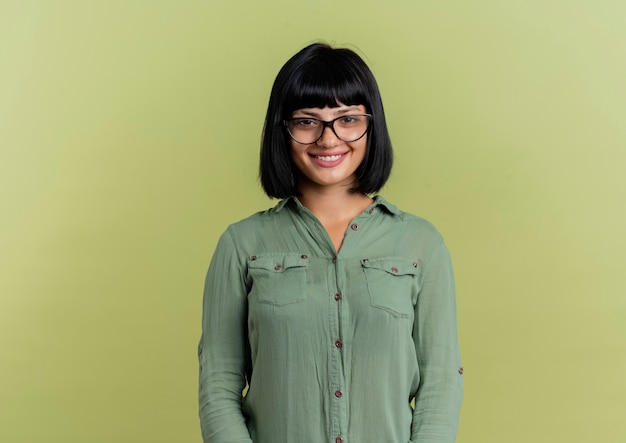 Photo gratuite souriante jeune fille brune caucasienne à lunettes optiques regarde la caméra isolée sur fond vert olive avec espace copie