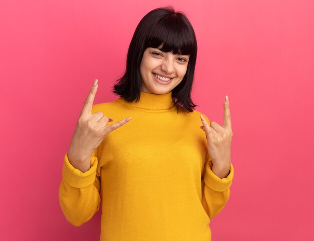 Souriante jeune fille caucasienne brune gestes cornes signe avec deux mains