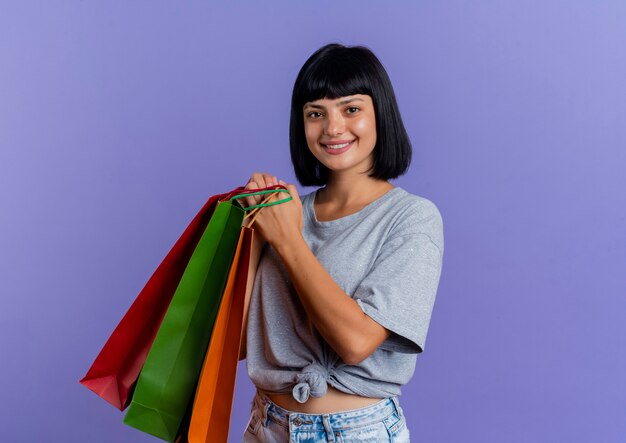 Souriante jeune fille caucasienne brune tient des sacs à provisions multicolores