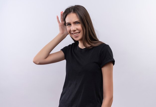 Souriante jeune fille caucasienne portant un t-shirt noir montrant le geste d'écoute sur fond blanc isolé