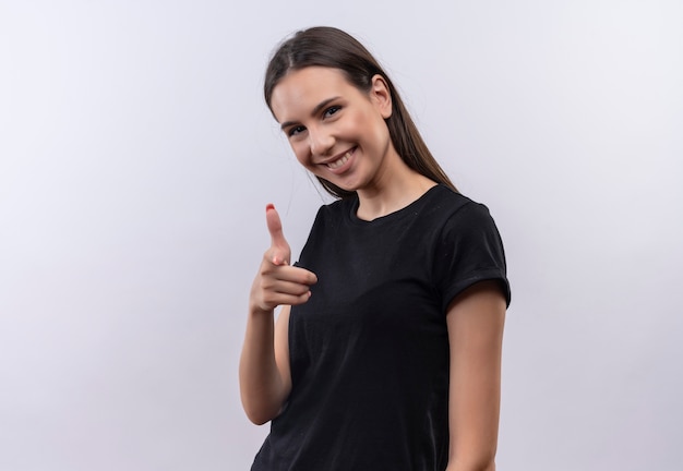 Souriante jeune fille caucasienne portant un t-shirt noir vous montrant le geste sur fond blanc isolé