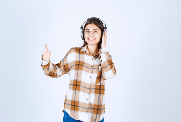 Souriante jeune fille dans les écouteurs écoutant la chanson et donnant des pouces vers le haut.