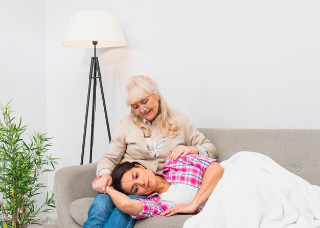 Souriante jeune fille dormant sur les genoux de sa mère âgée assise sur un canapé