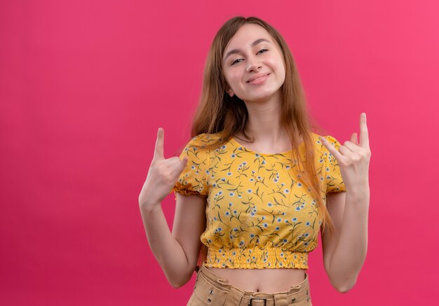 Souriante jeune fille faisant le geste de la roche sur un mur rose isolé avec espace de copie