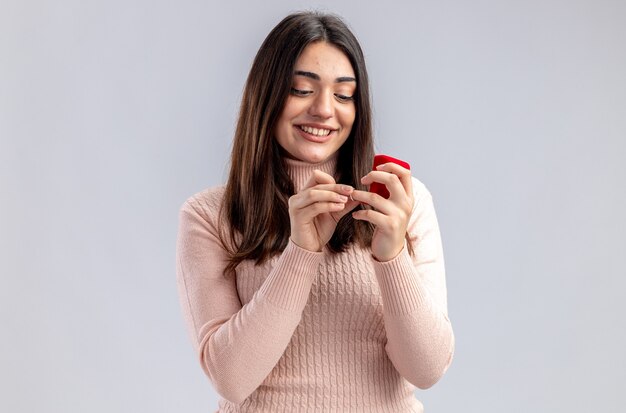 Souriante jeune fille le jour de la Saint-Valentin tenant et regardant la bague de mariage isolé sur fond blanc