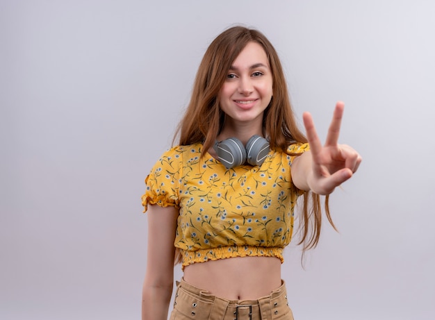 Photo gratuite souriante jeune fille portant des écouteurs sur le cou et faisant signe de paix sur un mur blanc isolé avec espace copie