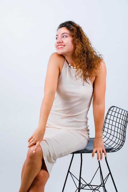 Souriante jeune fille regarde ailleurs en s'asseyant sur fond blanc