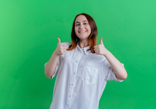 Souriante jeune fille rousse ses pouces vers le haut isolé sur vert