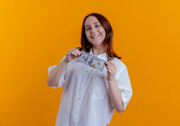 Souriante jeune fille rousse tenant de l'argent isolé sur jaune