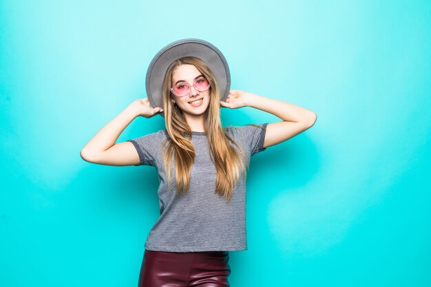 Souriante jeune fille en t-shirt de mode, chapeau et lunettes transparentes isolé sur fond vert