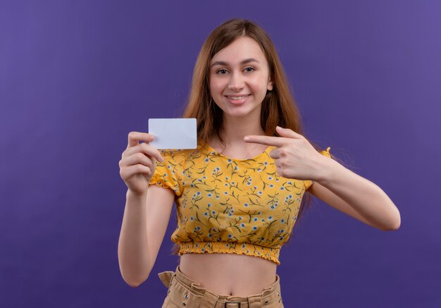 Souriante jeune fille tenant la carte et pointant vers elle sur un mur violet isolé