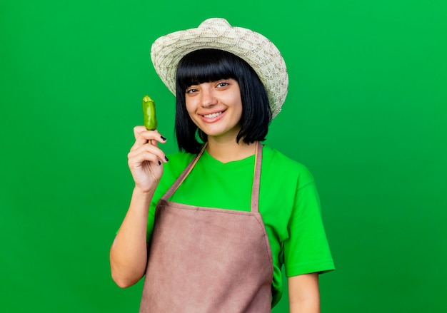 Souriante jeune jardinière en uniforme portant chapeau de jardinage détient poivre cassé