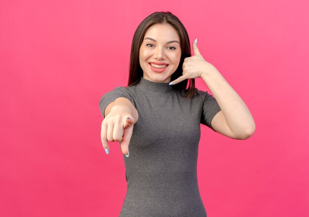 Souriante jeune jolie femme faisant le geste d'appel et pointant vers la caméra isolée sur fond rose avec espace de copie