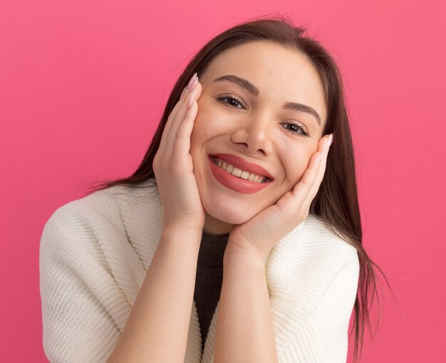 Souriante jeune jolie femme gardant les mains sur le visage