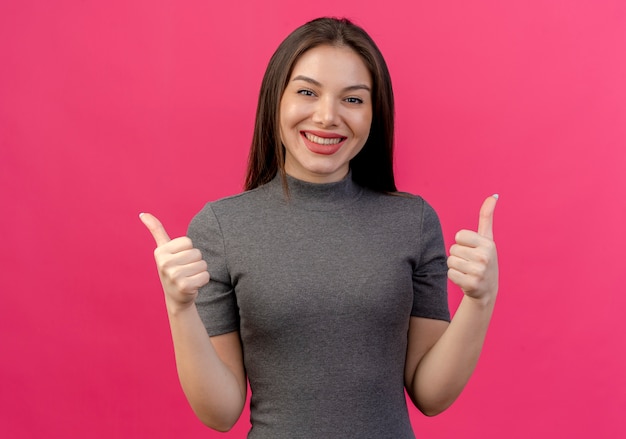 Souriante jeune jolie femme montrant les pouces vers le haut isolé sur fond rose