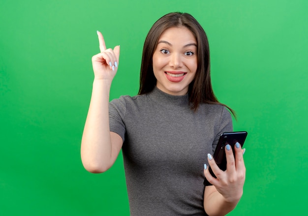 Souriante jeune jolie femme tenant un téléphone mobile et levant le doigt