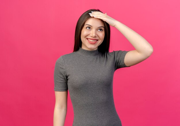 Souriante jeune jolie femme touchant la tête et levant isolé sur fond rose avec espace copie