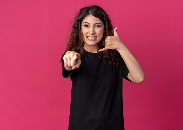 Souriante jeune jolie fille faisant un geste d'appel regardant et pointant vers la caméra