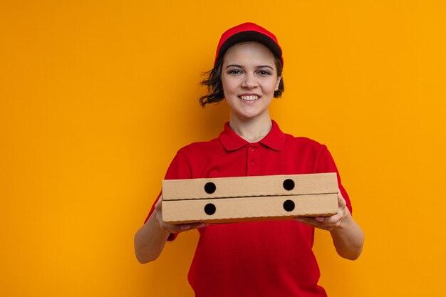 Souriante jeune jolie livreuse tient des boîtes à pizza