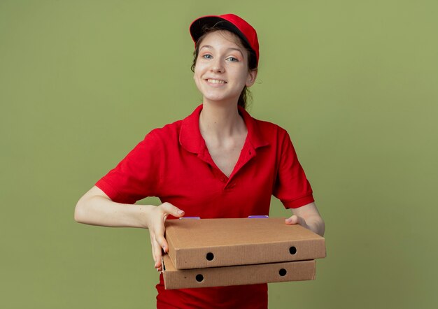 Souriante jeune jolie livreuse en uniforme rouge et chapeau tenant des paquets de pizza