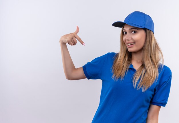 Souriante jeune livreuse portant l'uniforme bleu et le capuchon se pointe isolé sur un mur blanc avec espace de copie