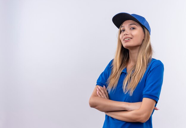 Souriante jeune livreuse portant l'uniforme bleu et une casquette croisant les mains isolés sur blanc