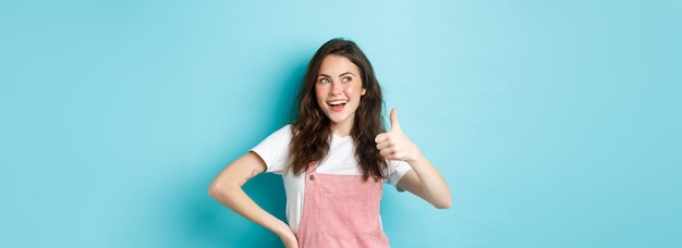 Souriante jolie adolescente avec un beau fard à joues et un maquillage glamour montrant le pouce vers le haut en signe d'approbation