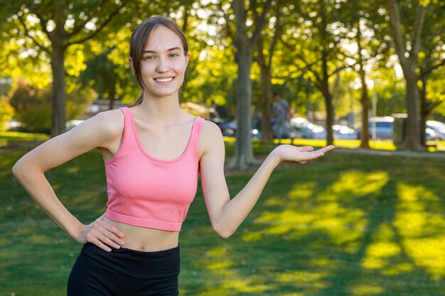 Souriante jolie fille tenant sa main ouverte en l'air et regardant la caméra au parc