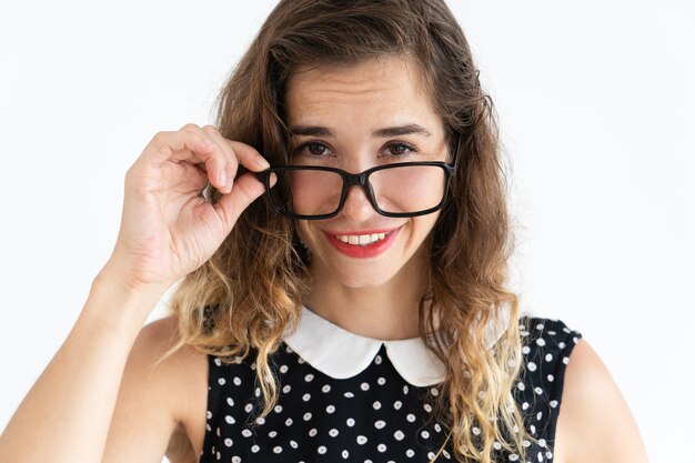 Souriante jolie jeune femme en ajustant les lunettes et en regardant la caméra au-dessus d&#39;eux