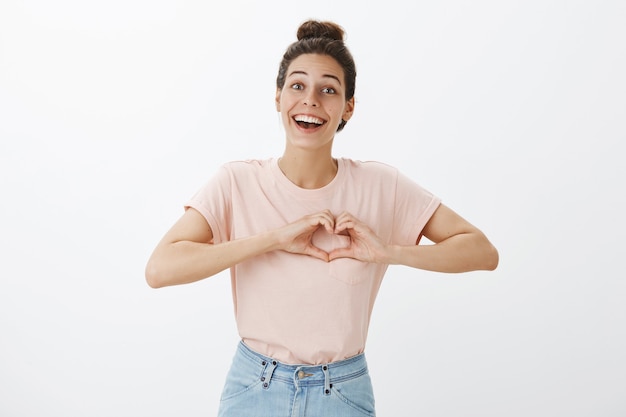 Souriante jolie jeune femme élégante posant contre le mur blanc