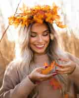 Photo gratuite souriante jolie jeune femme portant des feuilles d'érable diadème jouant avec les feuilles de l'automne