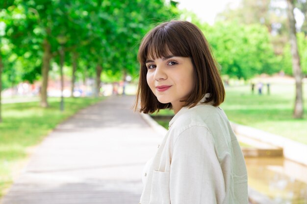 Souriante jolie jeune femme se présentant à la caméra dans le parc de la ville