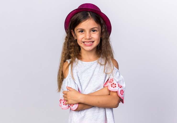 Photo gratuit souriante petite fille caucasienne avec chapeau de fête violet debout avec les bras croisés isolé sur mur blanc avec espace de copie