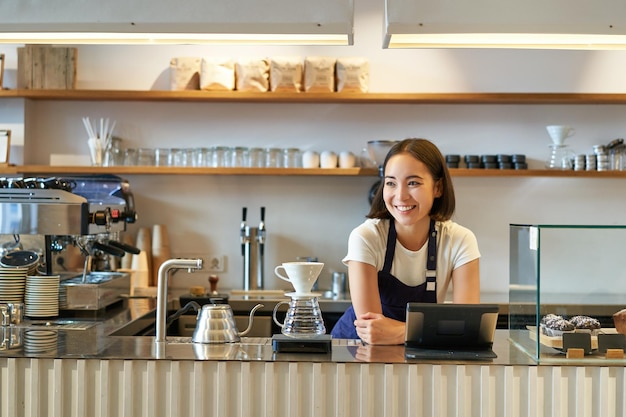 Souriante sympathique fille asiatique barista portant un tablier travaillant au comptoir brassant du café filtre gérant