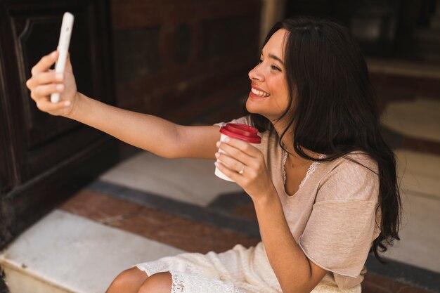 Sourire, adolescente, tenue, emporter, tasse café, prendre, selfie, depuis, téléphone portable