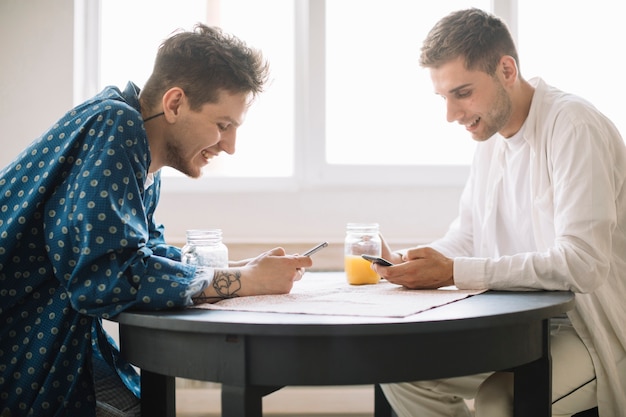 Photo gratuite sourire des amis à l'aide de téléphone portable tenant un pot de jus à la maison