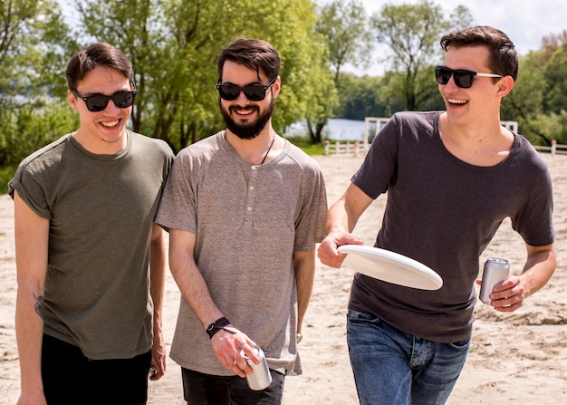 Sourire des amis de sexe masculin en lunettes de soleil marchant sur la plage