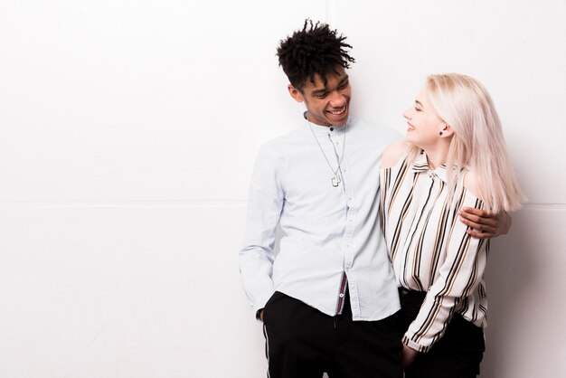 Sourire amoureux couple interracial embrassant debout contre le mur blanc