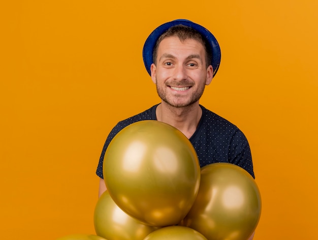 Sourire Bel Homme Caucasien Portant Chapeau De Fête Bleu Détient Des Ballons D'hélium Isolés Sur Fond Orange Avec Espace De Copie