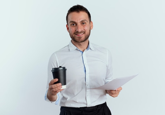 Sourire bel homme tient une tasse de café et des feuilles de papier isolés sur un mur blanc