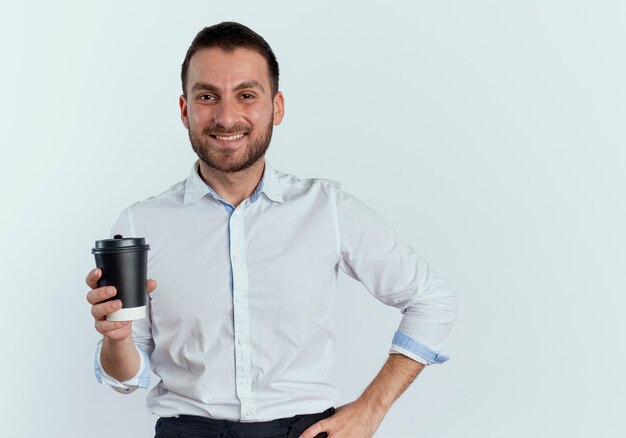 Sourire bel homme tient une tasse de café isolé sur un mur blanc