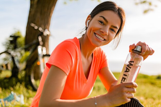 Sourire belle femme eau potable en bouteille faire du sport le matin dans le parc