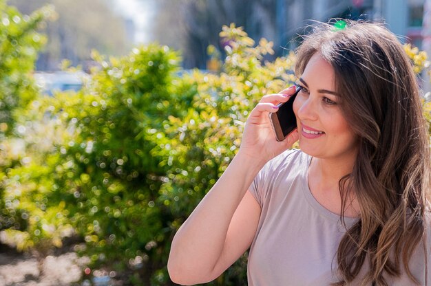 Sourire belle jeune femme parlant sur téléphone intelligent dans la ville. Technologie, communication, mode de vie et concept de personne - jeune femme souriante appelant un smartphone sur la rue de la ville