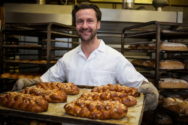 Photo gratuite sourire boulanger tenant miche de pains fraîchement sortis du four torsadées