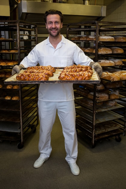 Sourire boulanger tenant miche de pains fraîchement sortis du four torsadées