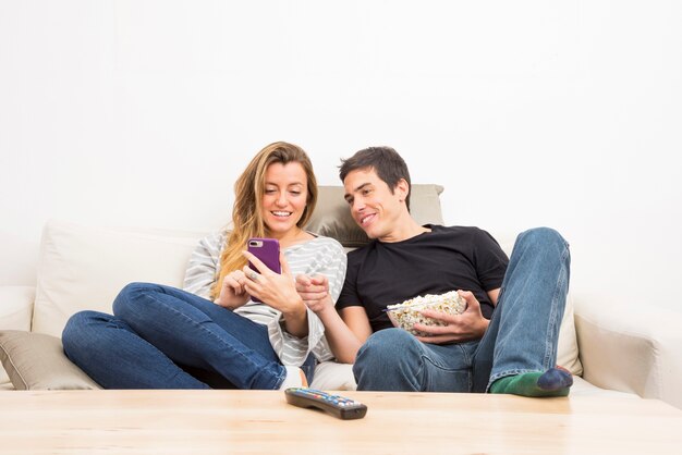 Sourire couple regardant un téléphone portable assis sur le canapé