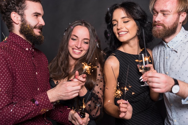 Sourire de dames et de gars tenant des feux de Bengale et un verre de boisson